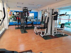 A gym with various exercise machines, a glass wall, and a wooden floor.