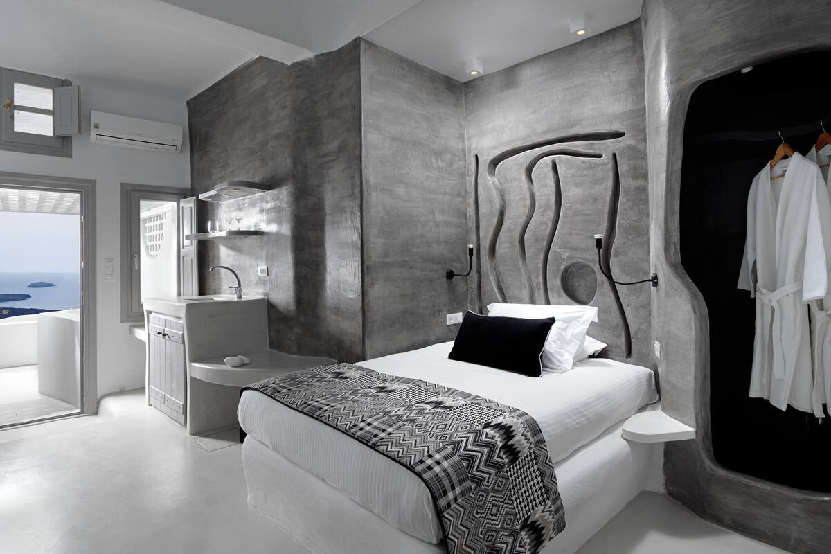 A modern bedroom with a large bed, a built-in vanity, and a view of the sea.