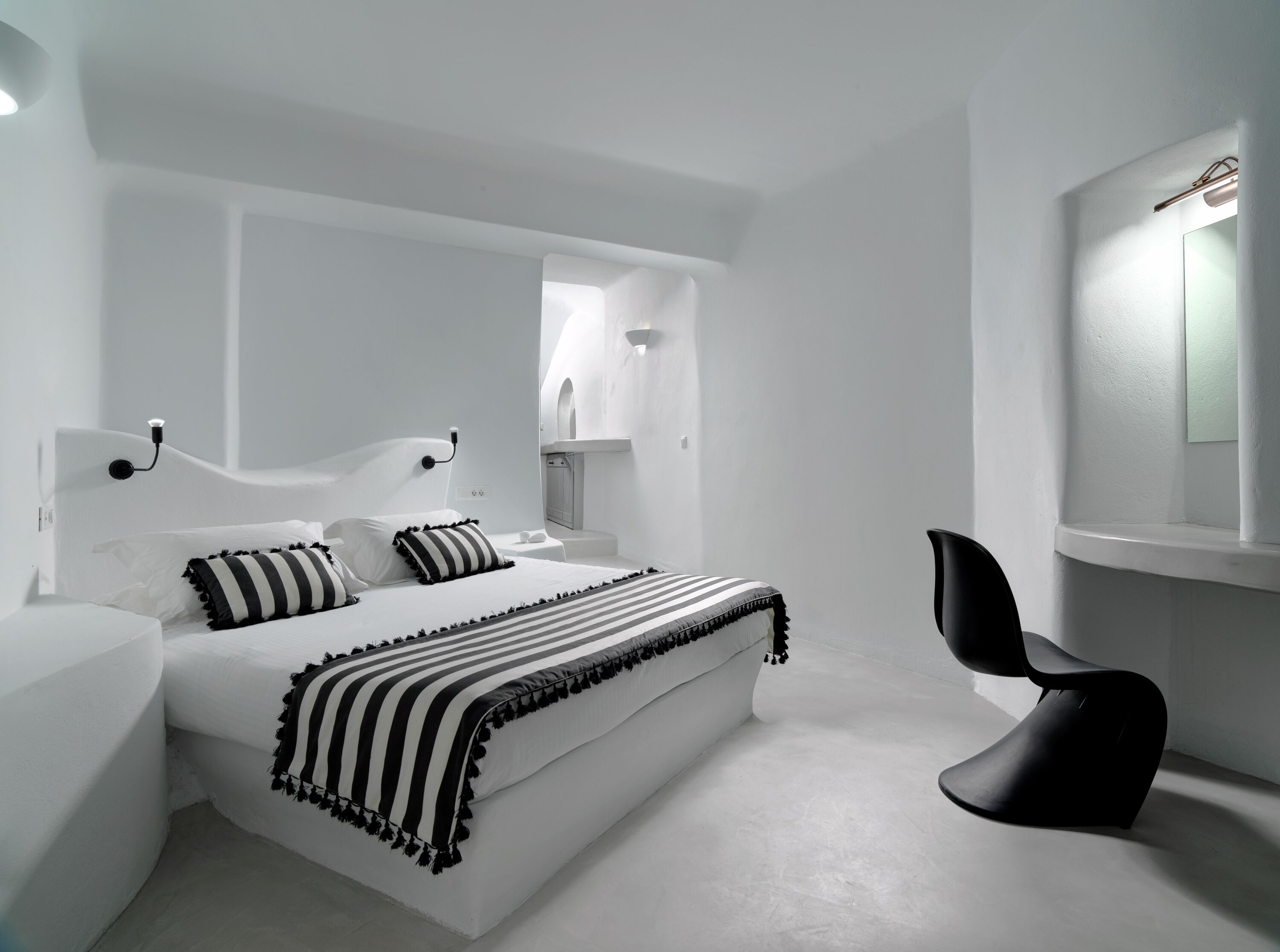 Un dormitorio moderno con una cama grande, una silla negra y una decoración en blanco.