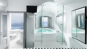 Un baño moderno con un jacuzzi de vidrio, un espejo grande y vistas al mar.