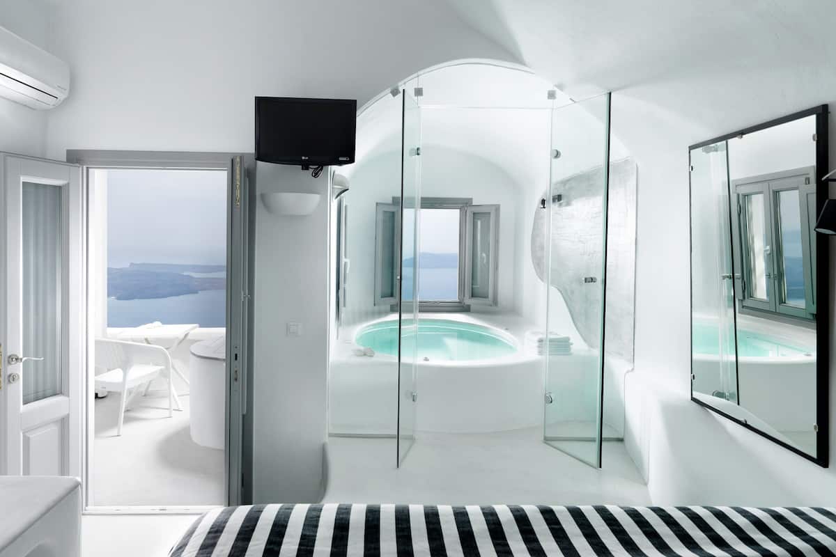 A modern bathroom with a glass-enclosed jacuzzi, a large mirror, and a view of the sea.