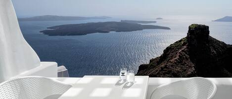 A table with two glasses and a bottle, overlooking a coastal view with rocky terrain and calm waters.