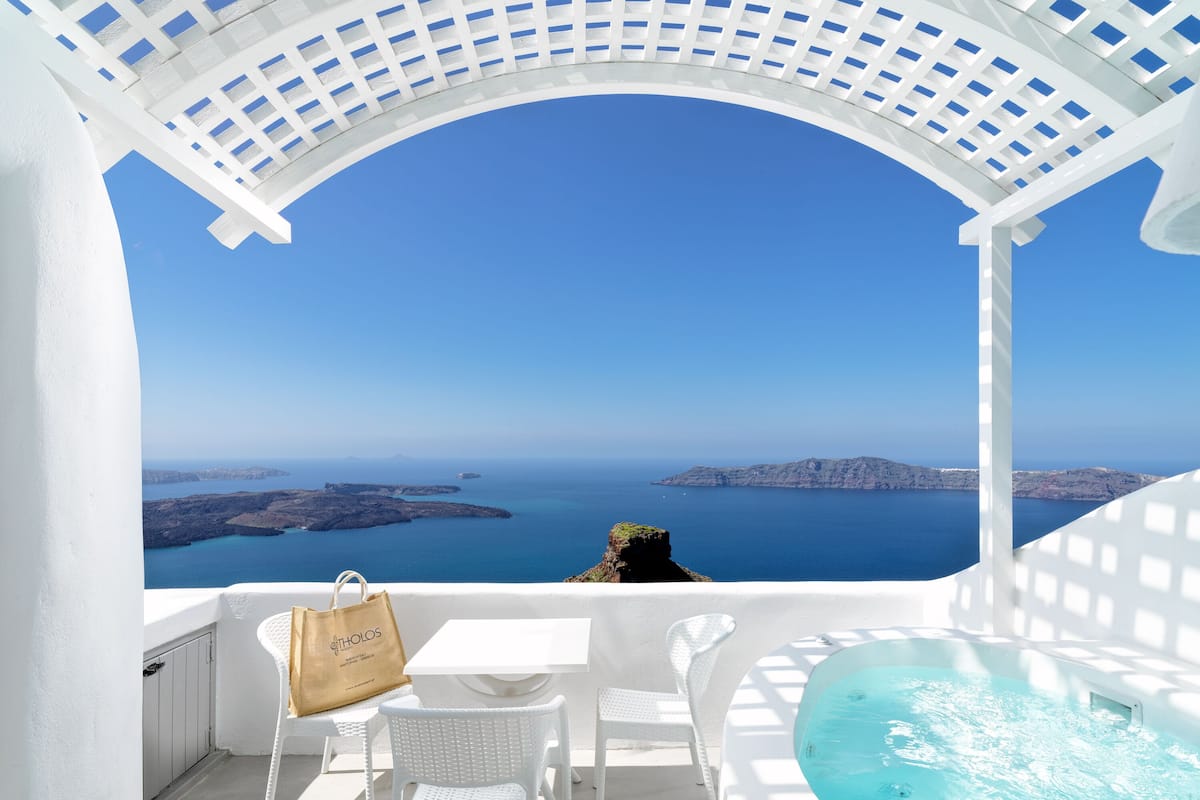 A white outdoor seating area with a view of the sea and islands.