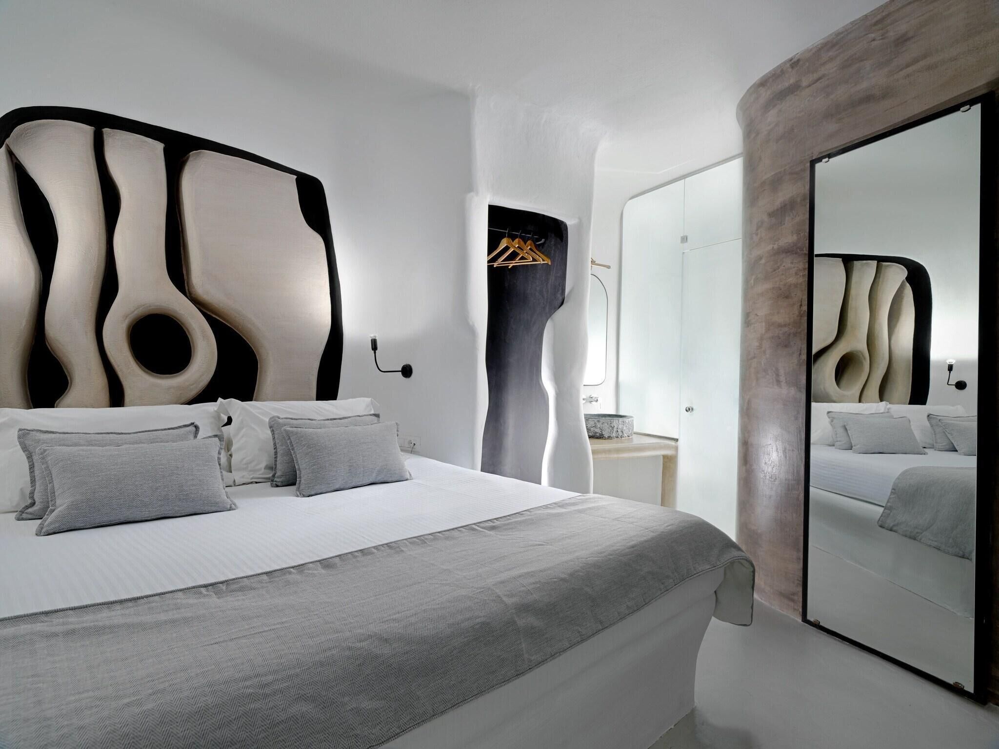 A modern bedroom with a unique headboard design, a large mirror, and a minimalist aesthetic.