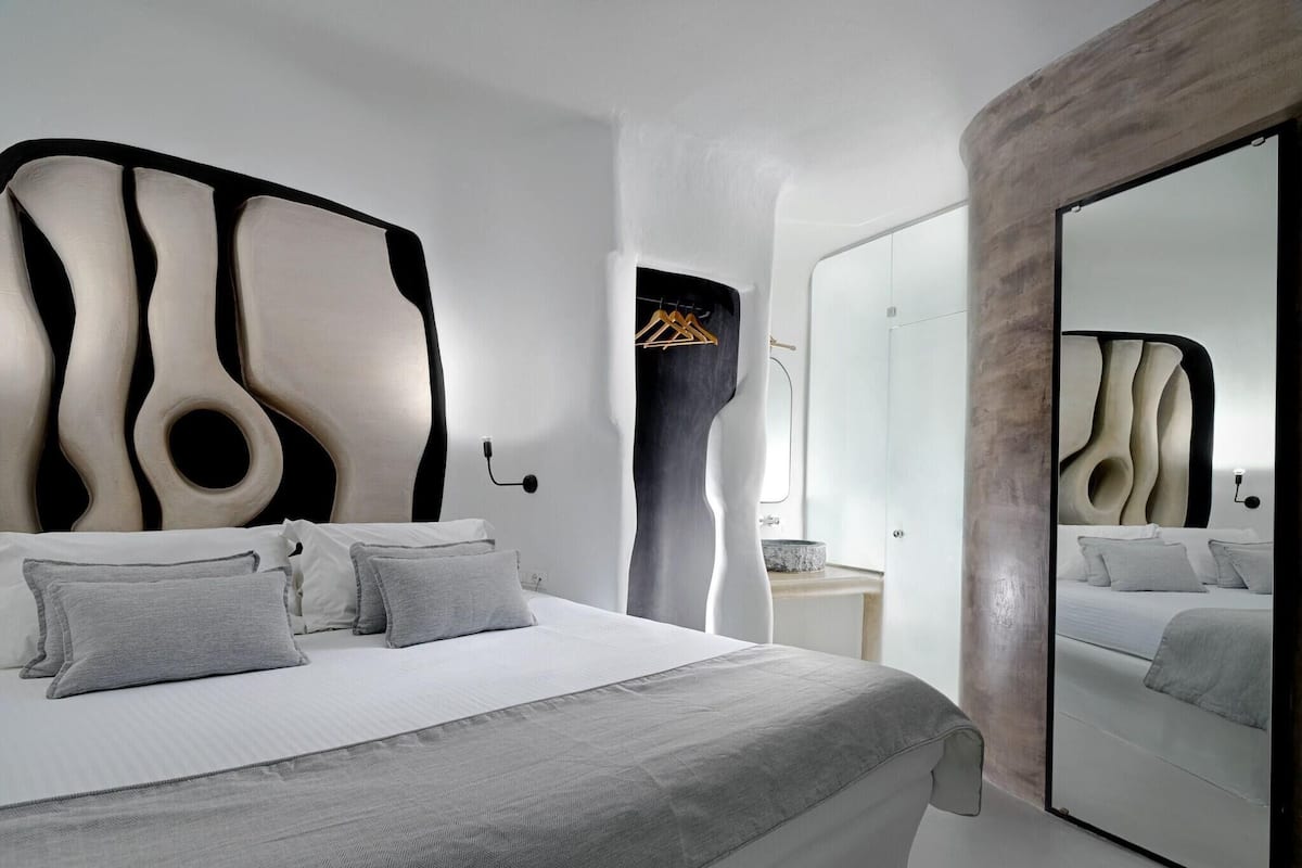 A modern bedroom with a unique headboard design, a large mirror, and a minimalist aesthetic.