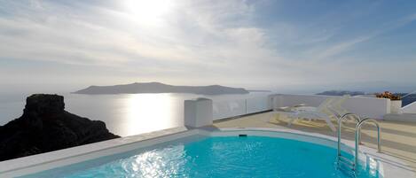 A swimming pool with a view of the sea and a rocky outcrop.
