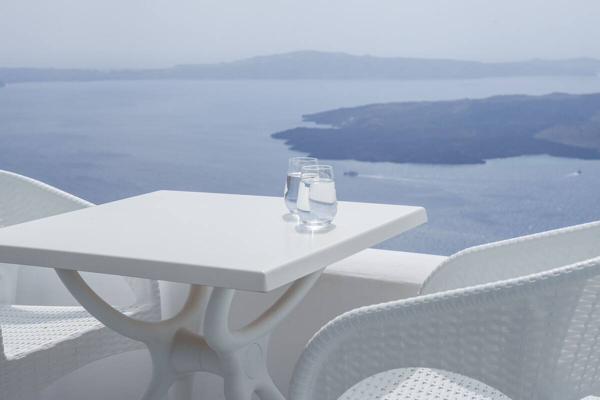 A white table with three glasses of water and a view of a calm sea and distant mountains.