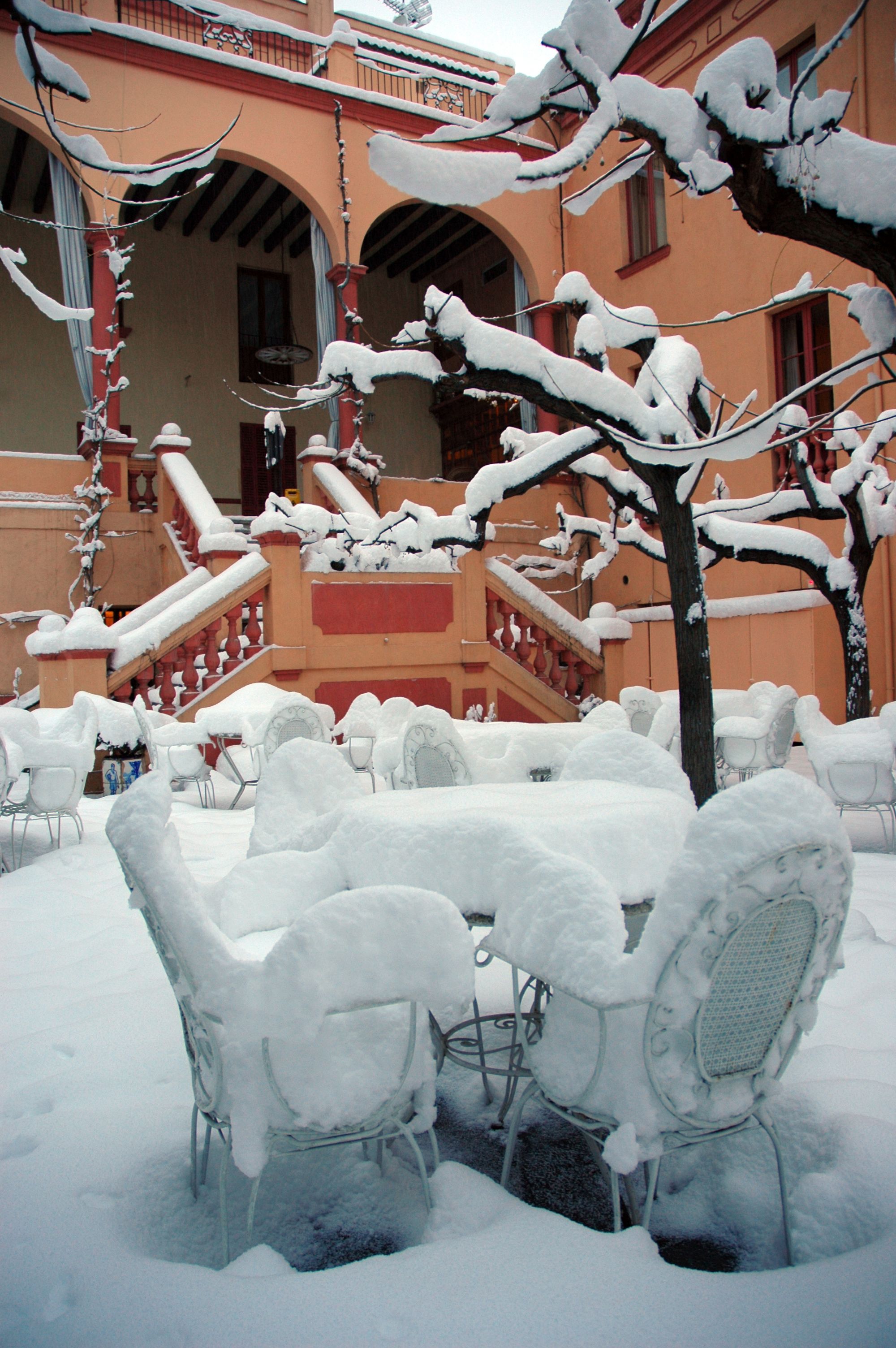 Outdoor seating area covered in snow, with a staircase and a building in the background.