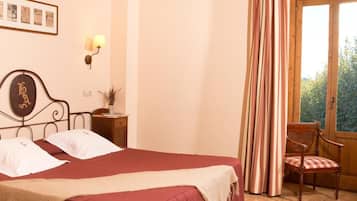 Un dormitorio con una cama grande, vigas de madera en el techo, una ventana con cortinas, una silla y una mesita de noche con una lámpara.