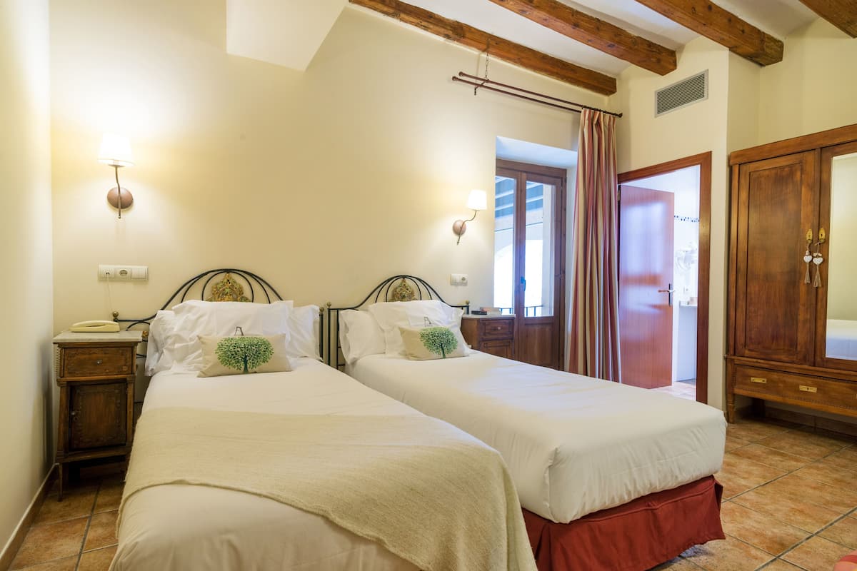 A bedroom with two beds, a wooden wardrobe, and a nightstand with a lamp.