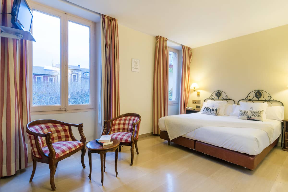 A hotel room with a bed, two chairs, a small table, and a window with curtains.