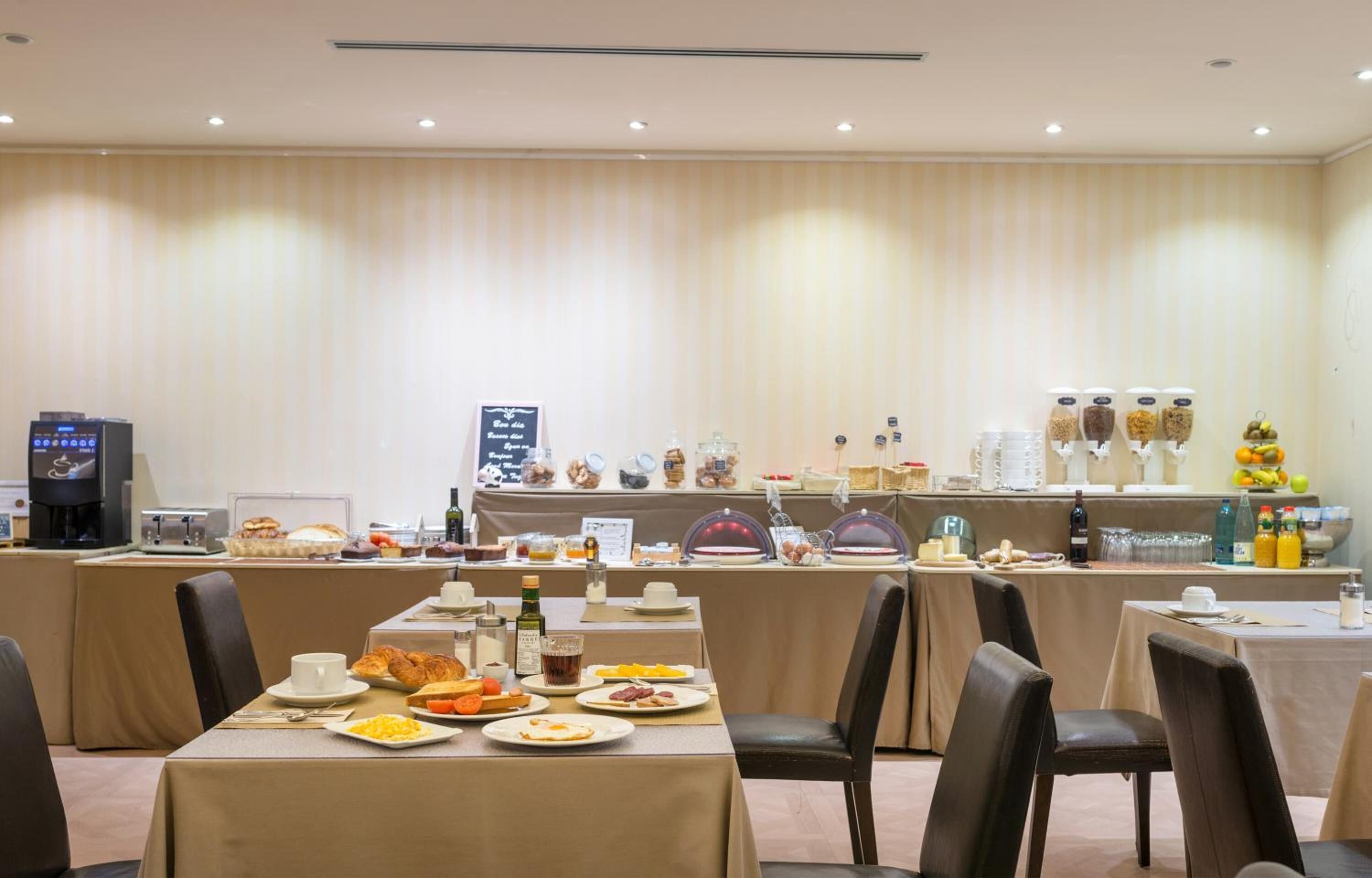 A breakfast buffet with various food items and beverages, a coffee machine, and a chalkboard menu.