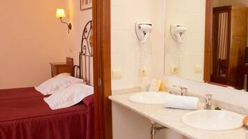 A hotel room with a bed, two sinks, a mirror, and a hairdryer.