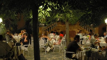 Un espace de restauration en plein air, avec des tables et des chaises, entouré d’arbres et d’un mur en pierre.