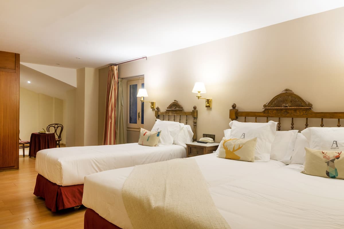 A hotel room with two beds, a wooden headboard, a nightstand with a lamp, and a chair.