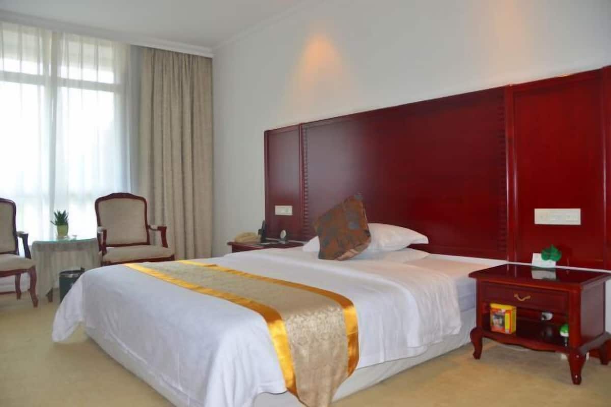A hotel room with a large bed, a nightstand, a chair, and a small table.