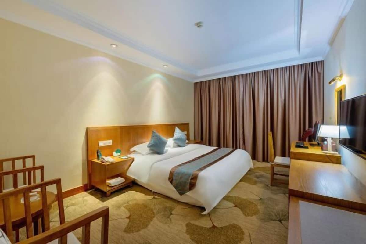 A hotel room with a bed, a desk, a chair, a TV, and curtains.