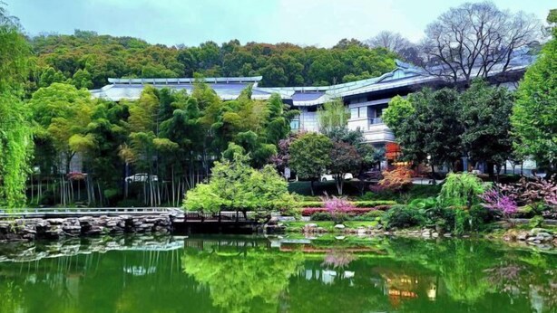 A traditional Japanese-style building with a pond in front, surrounded by lush greenery and trees. - Tieshan Hotel (Wuhu)