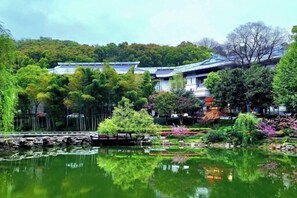 A traditional Japanese-style building with a pond in front, surrounded by lush greenery and trees. - Tieshan Hotel (Wuhu)