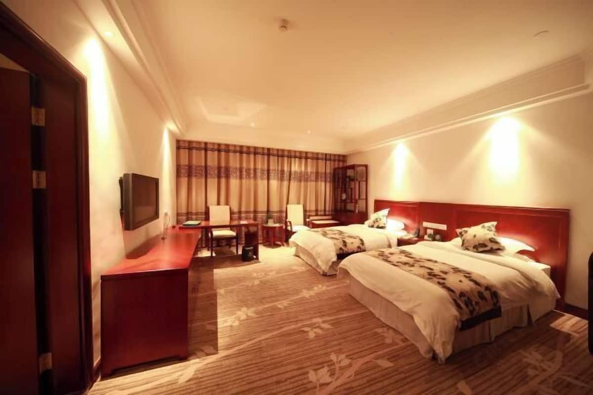 A hotel room with two beds, a desk, a TV, and a large window with curtains.