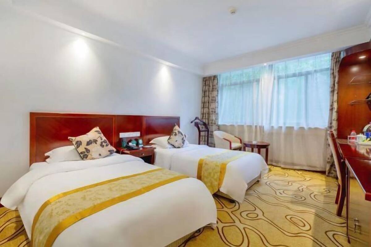 A hotel room with two beds, a desk, a chair, a small table, and a window with curtains.