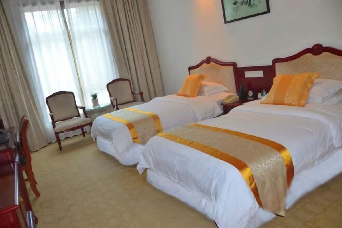 A hotel room with two beds, a desk, a chair, and a window with curtains.