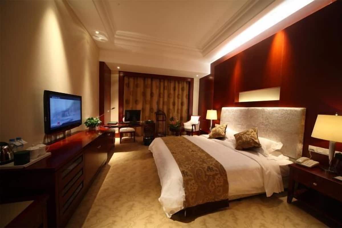 A hotel room with a large bed, a desk with a television, a desk lamp, and a chair.