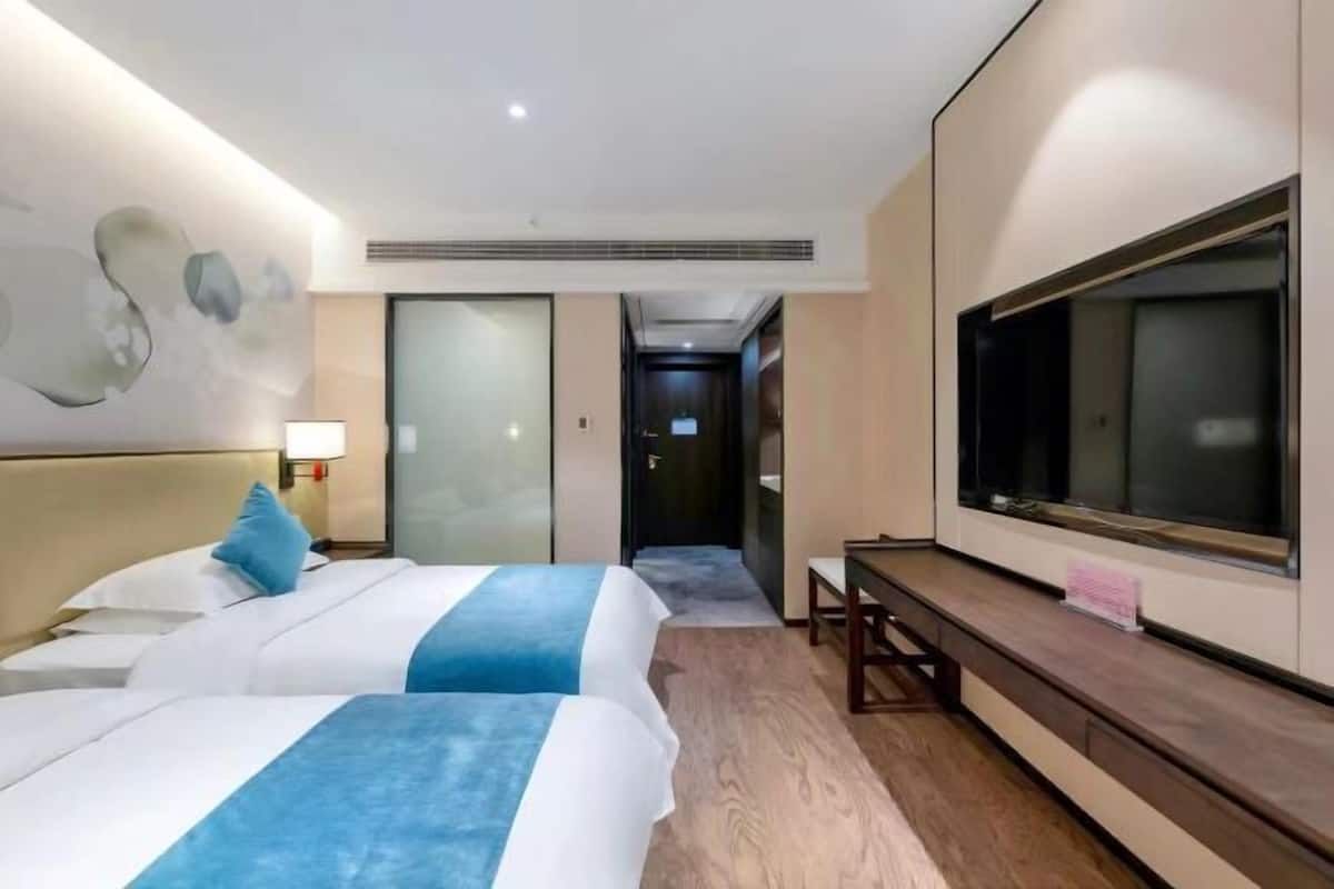A hotel room with two beds, a large TV, a desk, and a wall-mounted TV.
