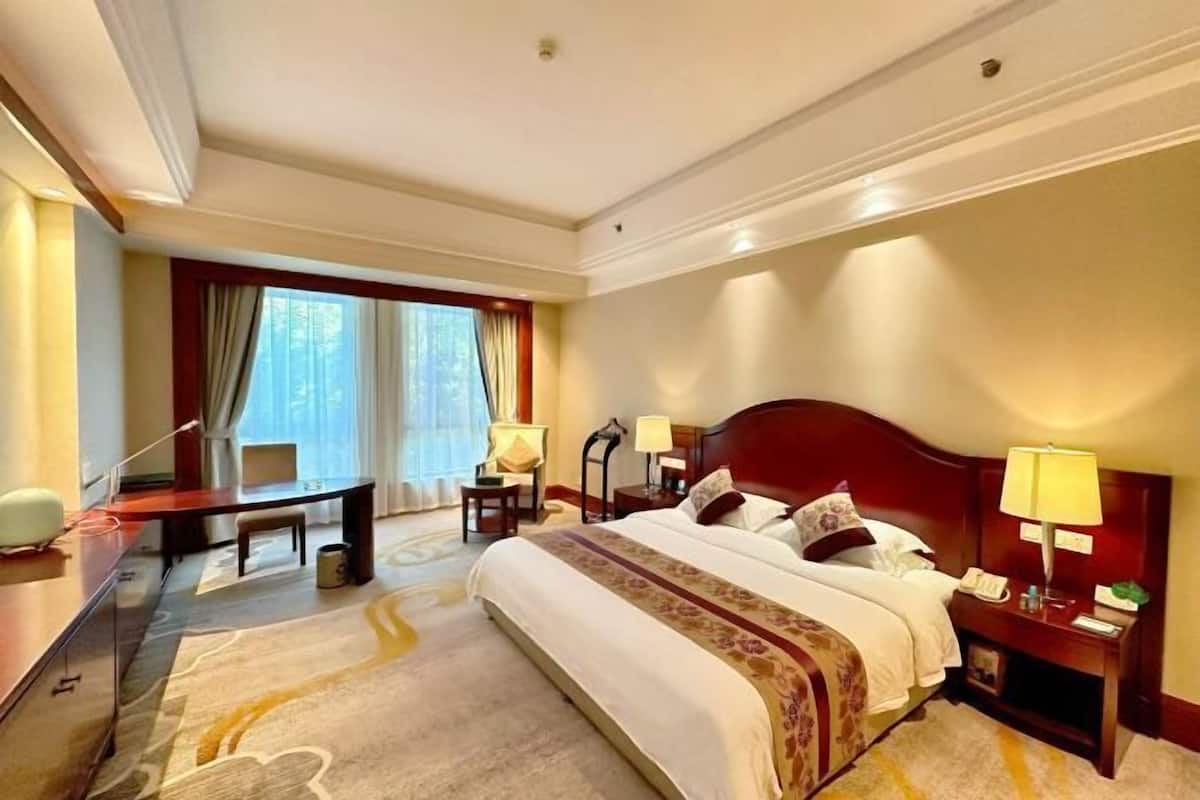 A hotel room with a large bed, a desk, a chair, a lamp, and a window with curtains.