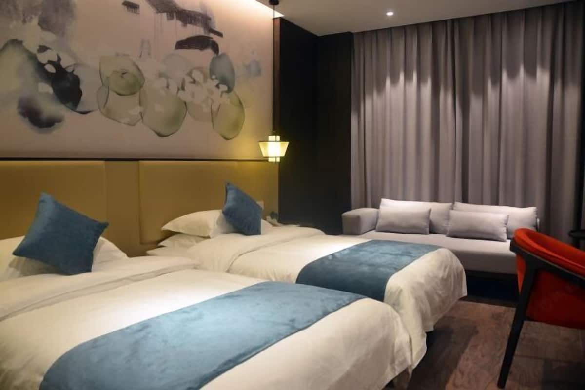 A hotel room with two beds, a sofa, a red chair, and a painting on the wall.