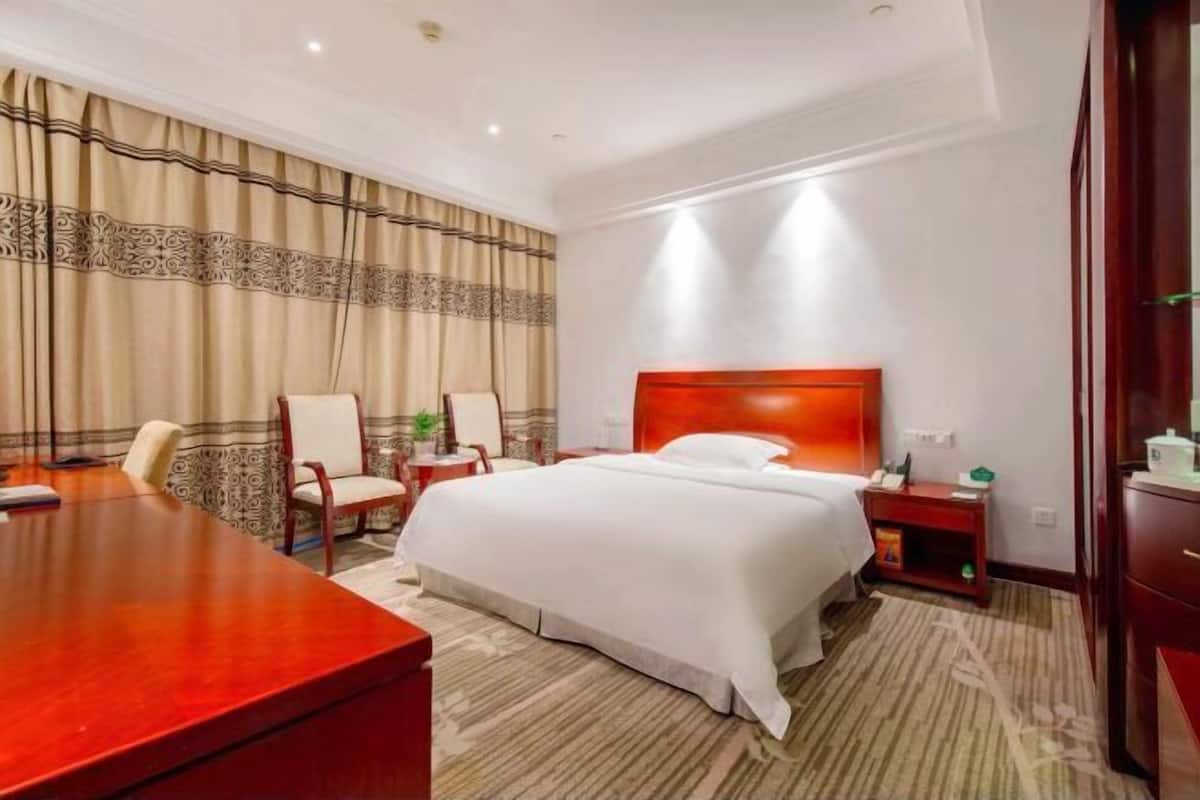 A hotel room with a large bed, two chairs, a desk, and a nightstand.