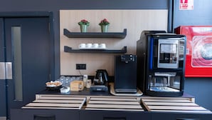 Een moderne koffiehoek met een koffiezetapparaat, een telefoon en een waterkoker op een houten tafel.