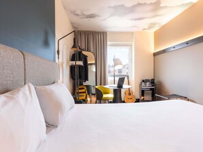 A hotel room with a bed, a desk with a laptop, a guitar, a chair, and a window with curtains. - ibis Malaga Centro Ciudad (Málaga)