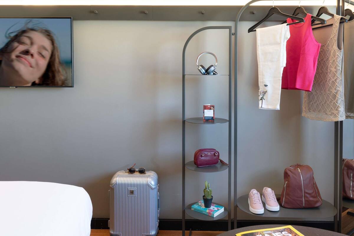 Une chambre d’hôtel équipée d’un lit, d’un téléviseur fixé au mur, d’un porte-bagages et d’une étagère pour les effets personnels.