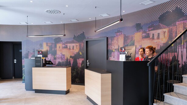 Een modern ingerichte receptie met een groot scherm, een receptiebalie en een trap.
