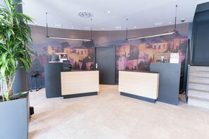 Un espace d’accueil moderne comprenant deux comptoirs de réception, un grand écran numérique mural et une plante en pot.