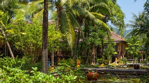 A tropical resort with lush greenery, a pond with lily pads, and a building with a tiled roof. - Princess Kamala Beachfront Hotel Phuket (Kamala)