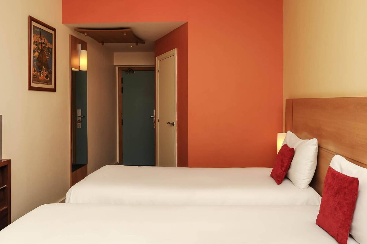 A hotel room with two beds, a wooden headboard, and a door leading to another room.