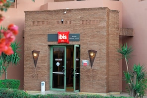 Un edifici de maó amb una entrada de porta de vidre, un rètol que diu "ibis Hotels" i dues làmpades fixades a la paret.