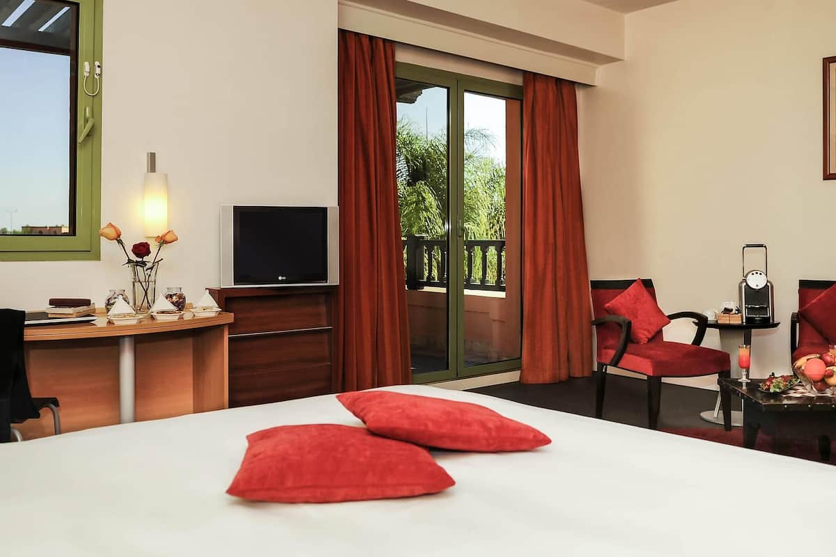 Una camera d'albergo con un letto, una scrivania con televisore, una sedia e un tavolo con lampada e fiori.