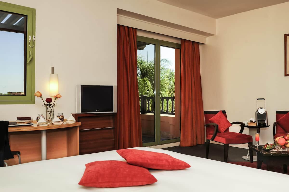 A hotel room with a bed, a desk with a TV, a chair, and a window with curtains.