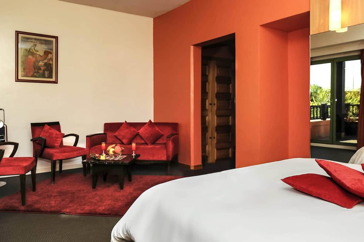 Una camera d'albergo con un letto, due divani rossi, un tavolino da caffè con della frutta e un quadro appeso al muro.