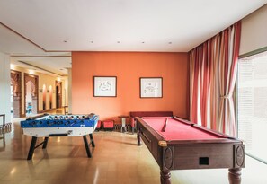 A pool table and foosball table in a room with orange walls and striped curtains. - ibis Marrakech Palmeraie Hotel (Marrakech)