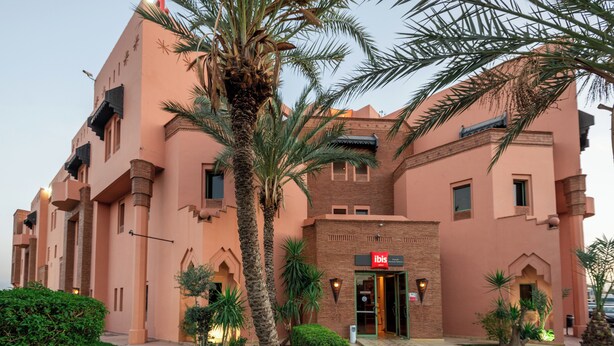 A hotel with a pink facade, palm trees, and a sign reading "ibis." - ibis Marrakech Palmeraie Hotel (Marrakech)