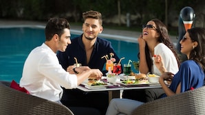 Un grupo de personas cenando al aire libre junto a una piscina, con una mesa dispuesta para una comida.