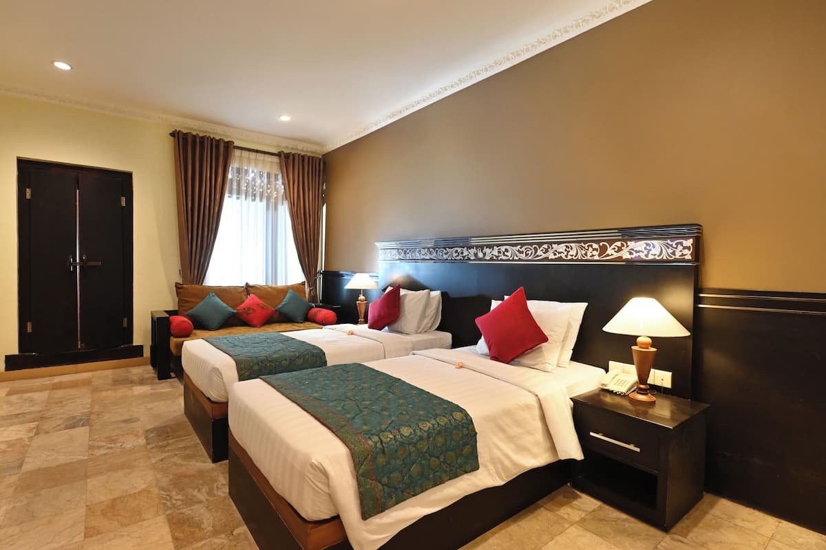 A hotel room with two beds, a nightstand with a lamp, a telephone, and a door.