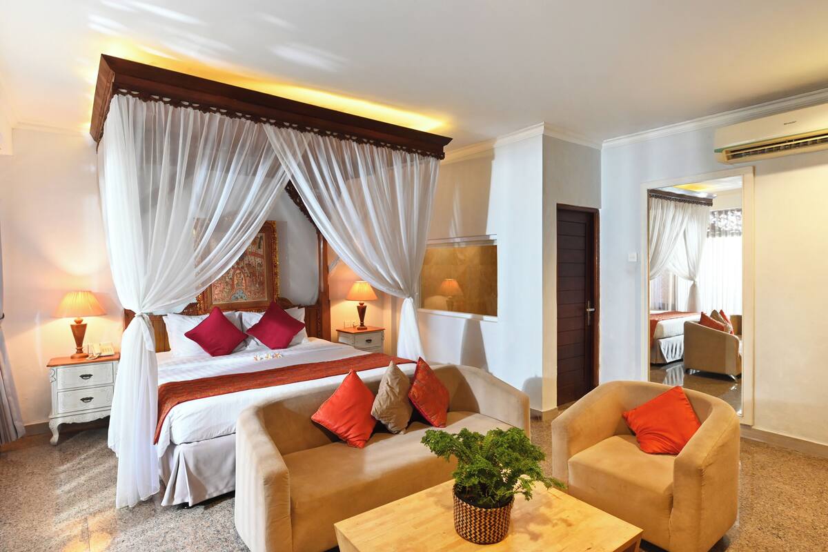 A hotel room with a bed, two bedside tables with lamps, a sofa, a coffee table, and a potted plant.
