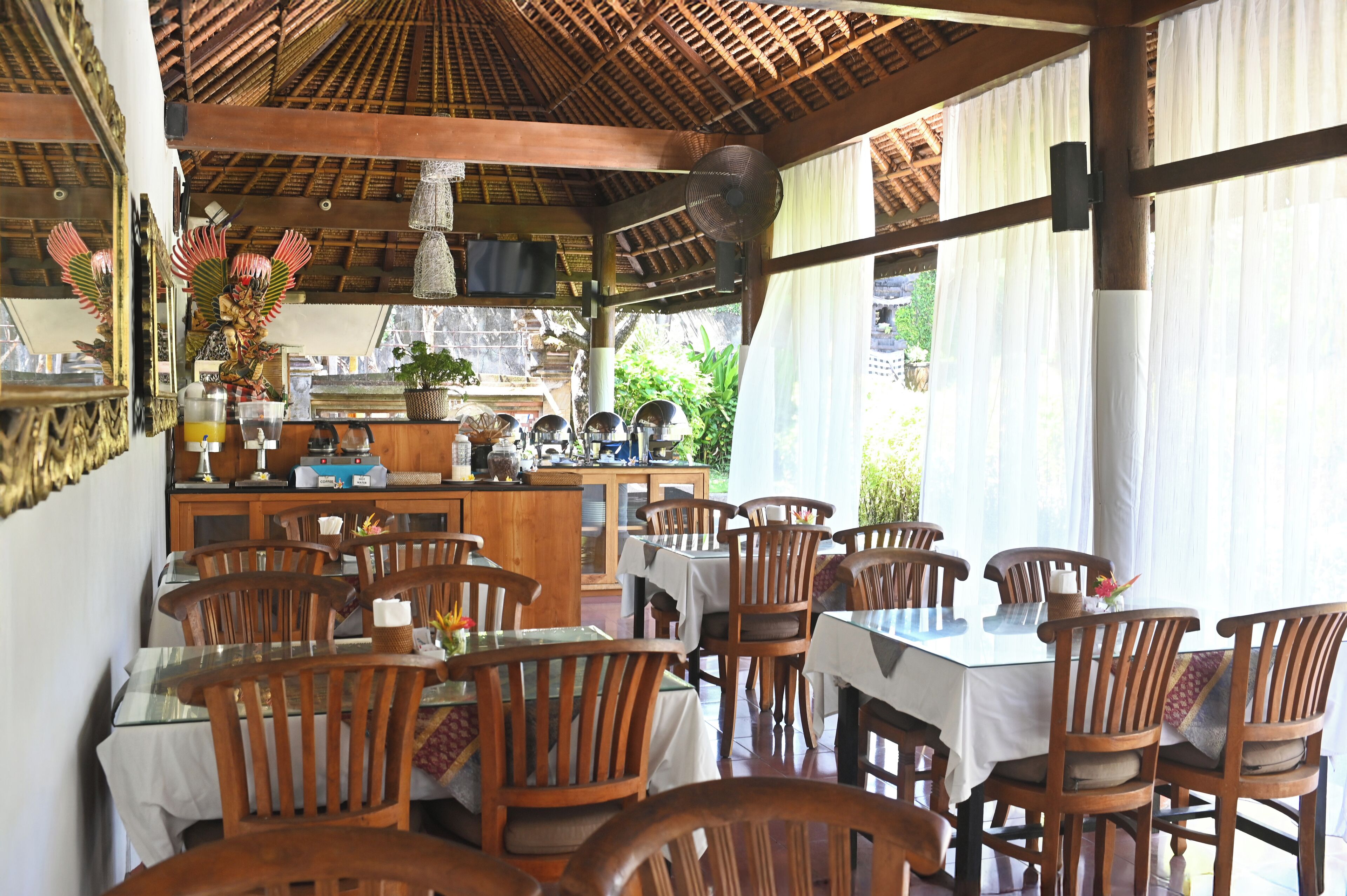 A restaurant with wooden tables and chairs, a bar area, and a view of greenery outside.