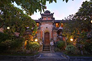 A traditional building with a central wooden door, surrounded by lush greenery and stone decorations. - Puri Dewa Bharata Hotel & Villas (Seminyak)