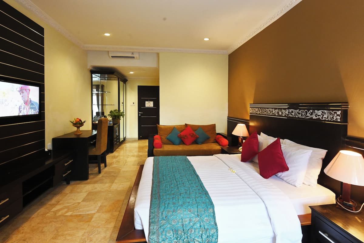 A hotel room with a large bed, a TV, a desk with a chair, and a sofa.